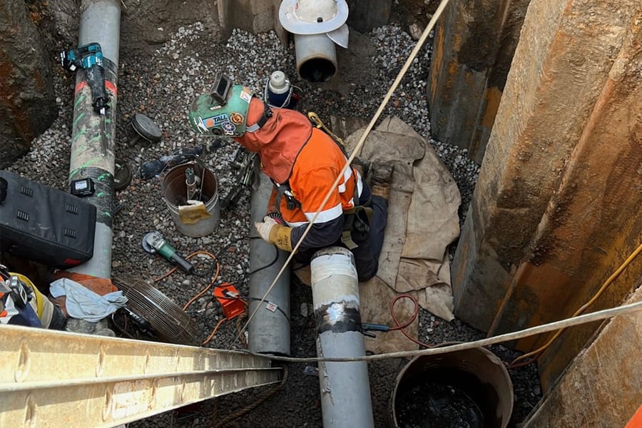 Worker welding underground pipeline inside deep trench